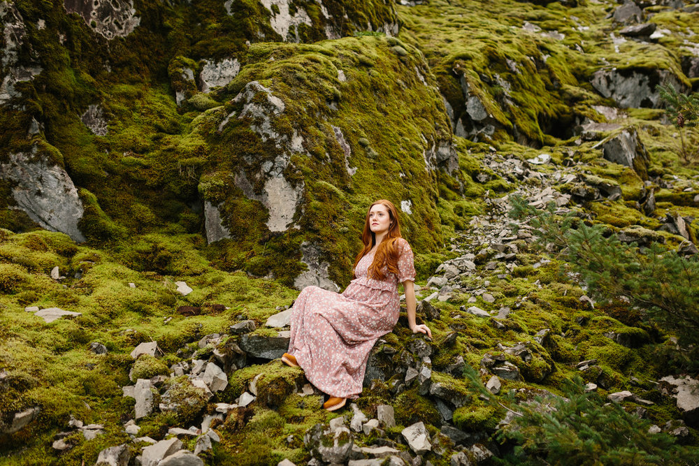 A beautiful, red-haired woman sitting on mossy rocks