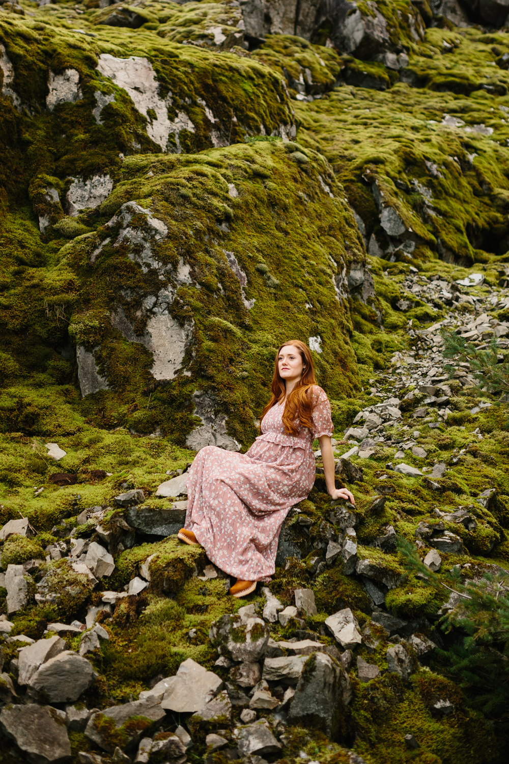 A beautiful, red-haired woman sitting on mossy rocks