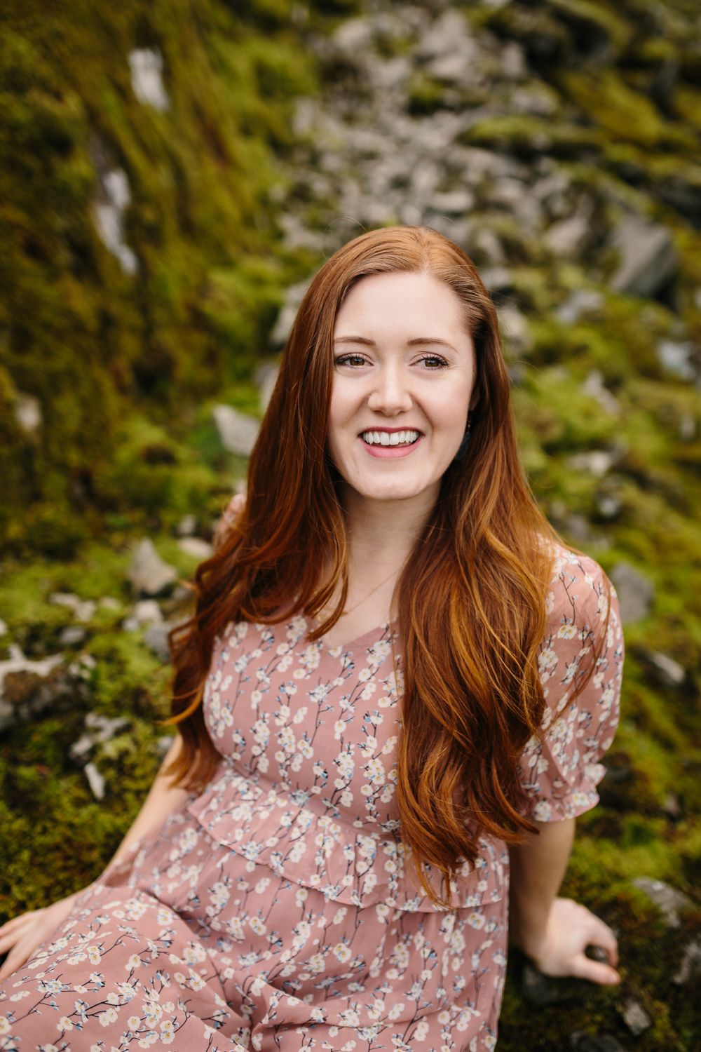 Portrait of a happy, red-haired woman sitting on mossy rocks