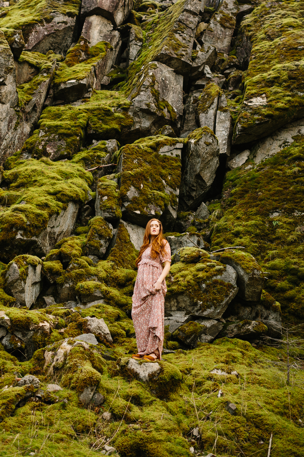 Portrait of a beautiful red-haired woman standing on mossy bould