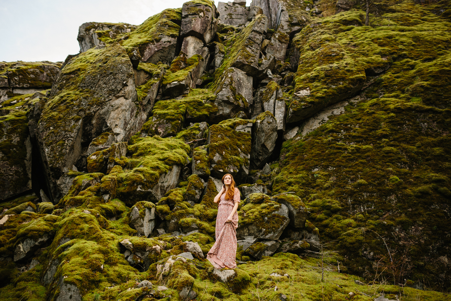 Portrait of a beautiful red-haired woman standing on mossy bould