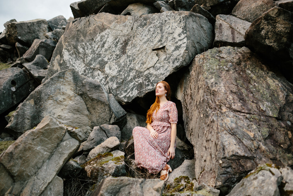 A Portrait of a Beautiful, Red-Haired Woman Sitting Amidst Bould