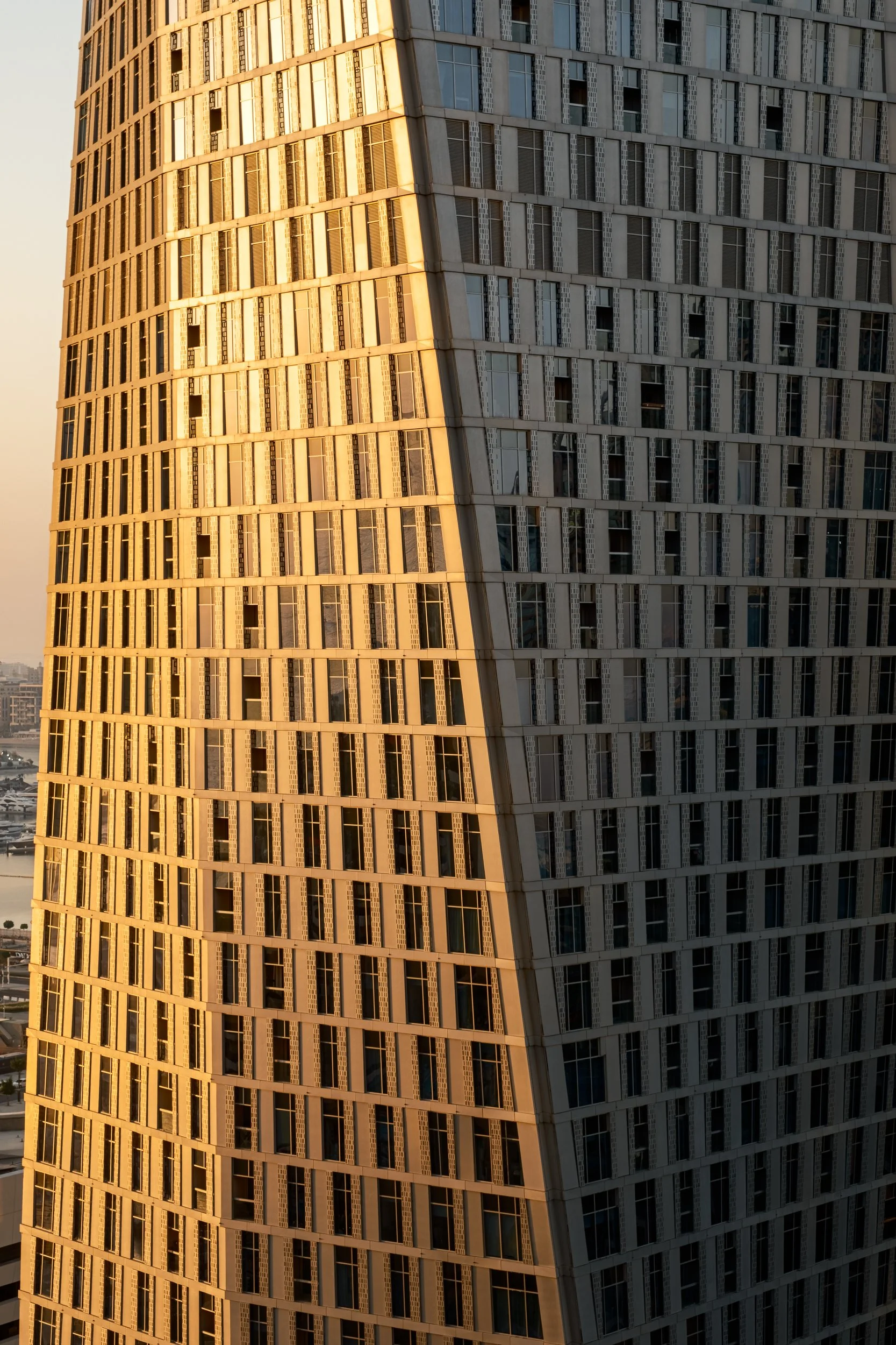 Close-up of a modern skyscraper with a grid-like window pattern, reflecting the golden sunset light.
