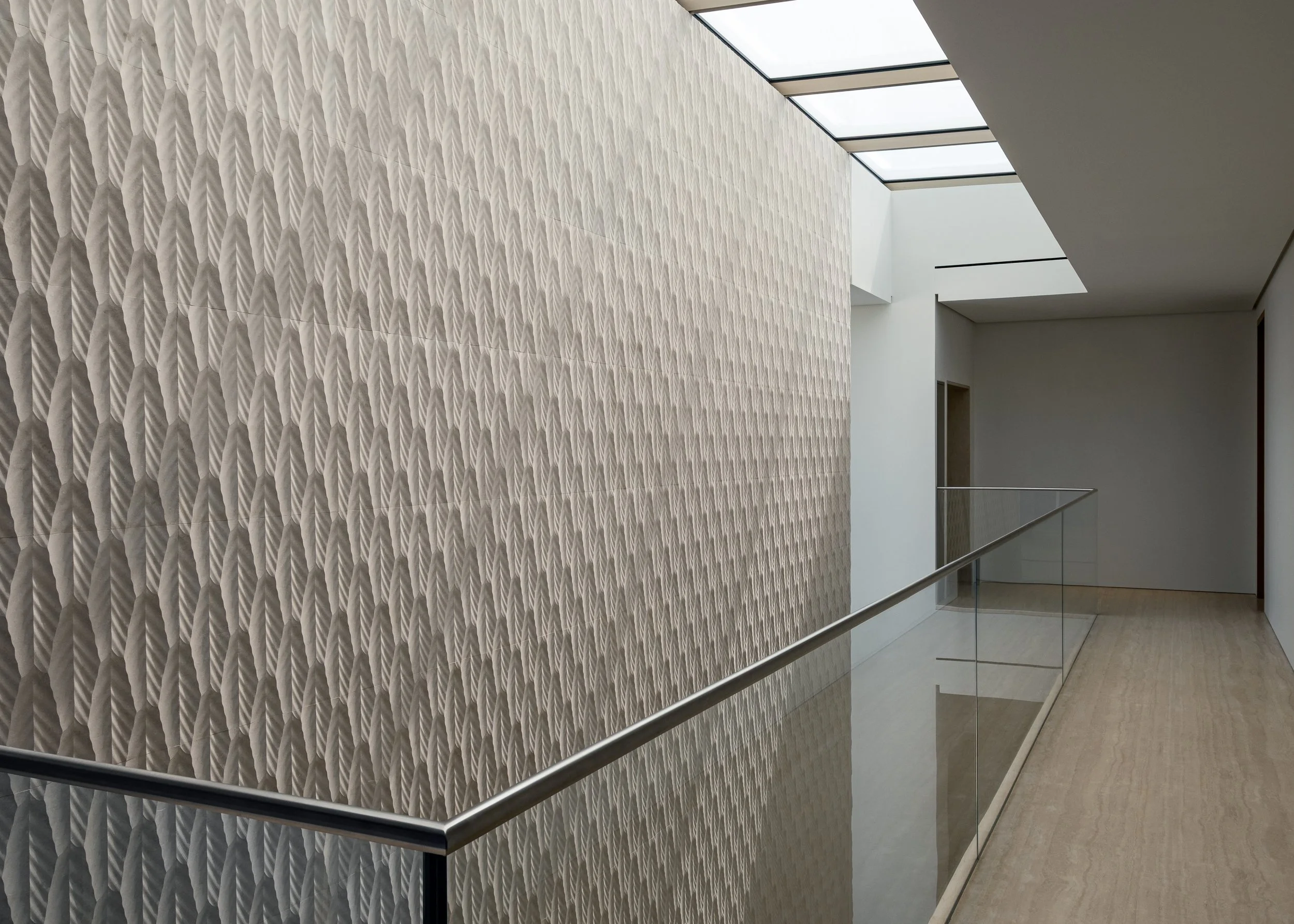 Interior view of a modern building with a textured wall, a glass ceiling, and a metal railing along a corridor.