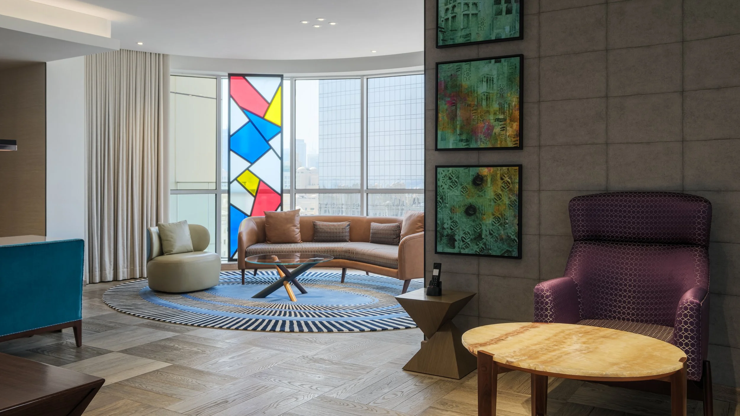Modern hotel lobby with colorful furniture, abstract art on a tiled wall, and a large window with a stained glass panel showing cityscape.