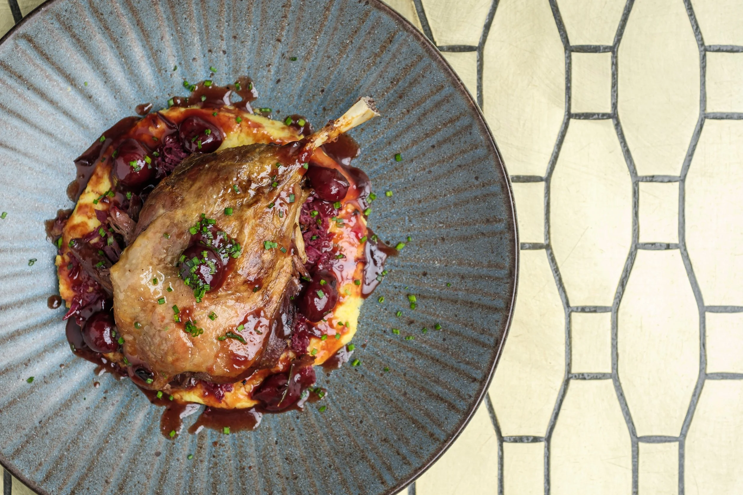 A plated dish with cooked duck breast topped with a cherry sauce and sprinkled with chopped chives.