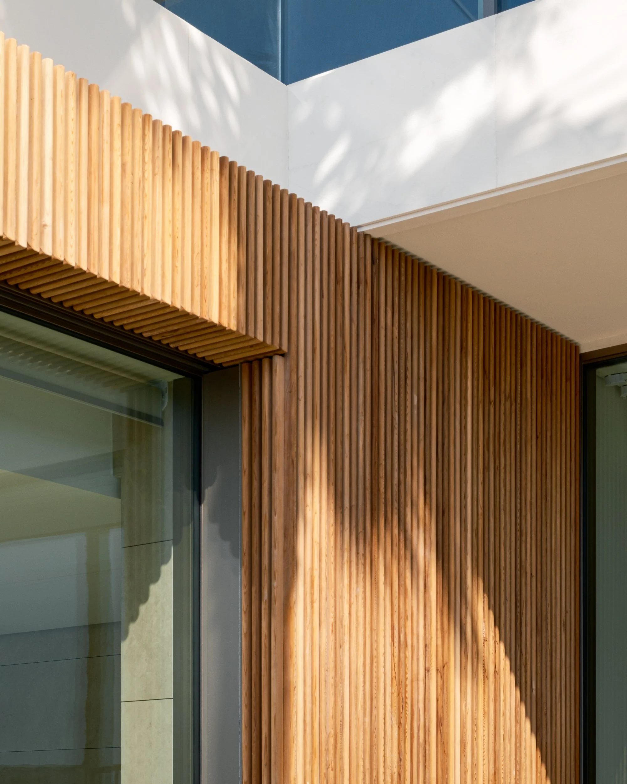 Close-up of a modern wooden slatted wall with shadow patterns and glass window reflections.