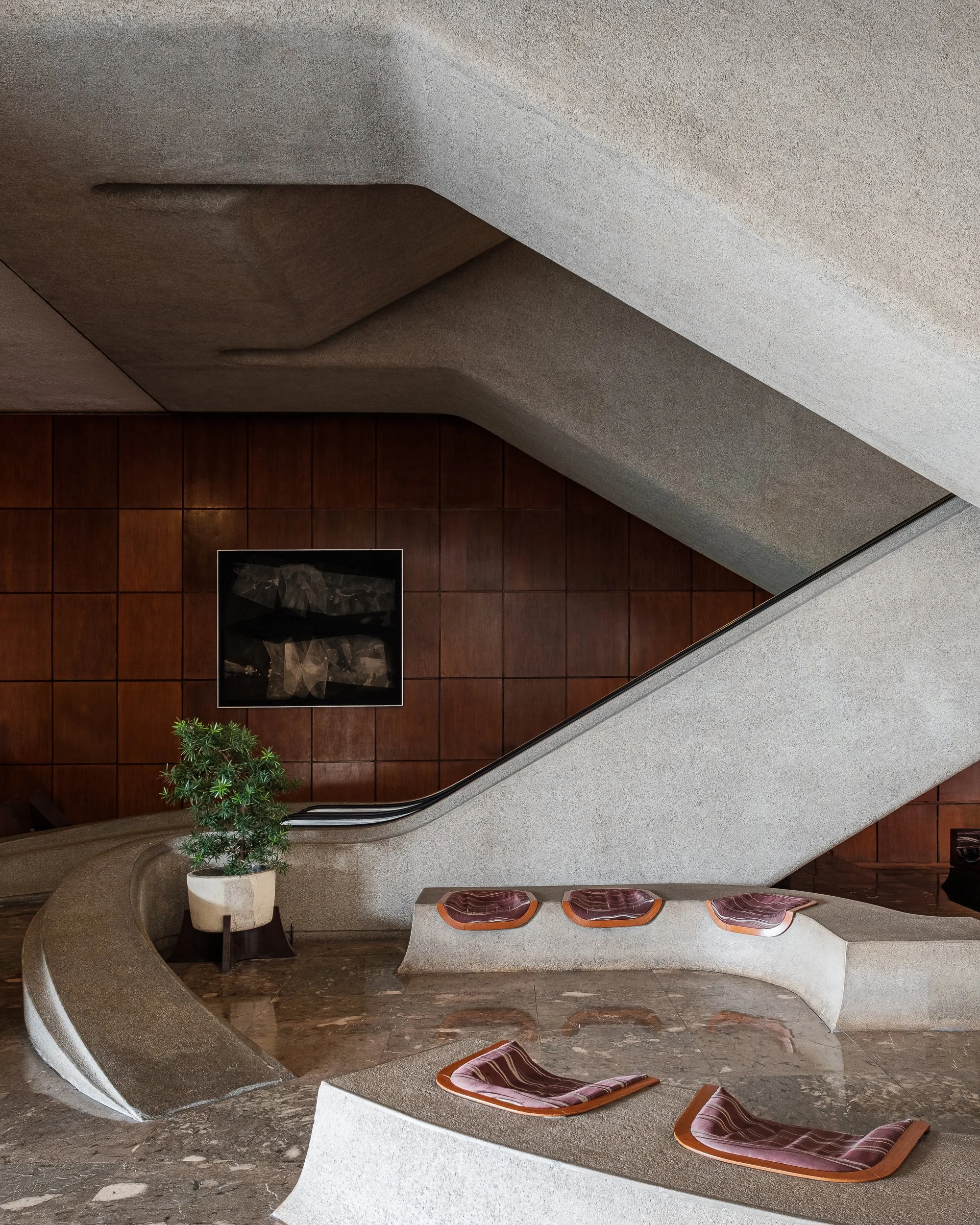 A modern, curved sitting area with built-in seats and wooden paneling on the wall. There is a potted plant and a framed artwork on the wall.