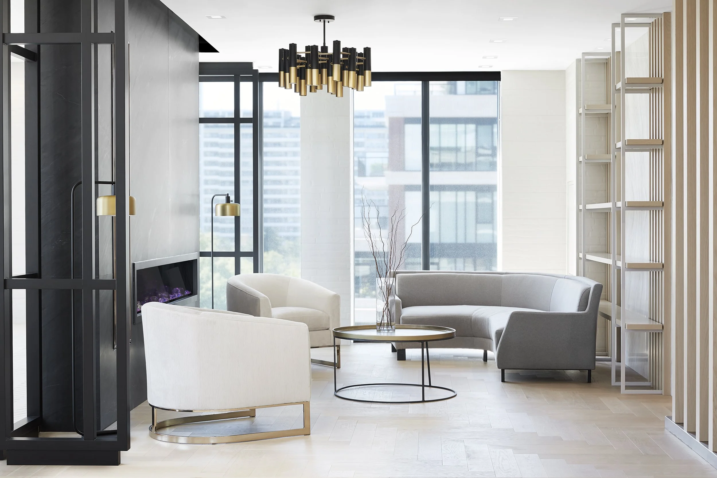 Modern party lounge at Mattamy Homes - J. Davis House, with light-coloured furniture, large windows, a black and gold chandelier, and decorative shelving.