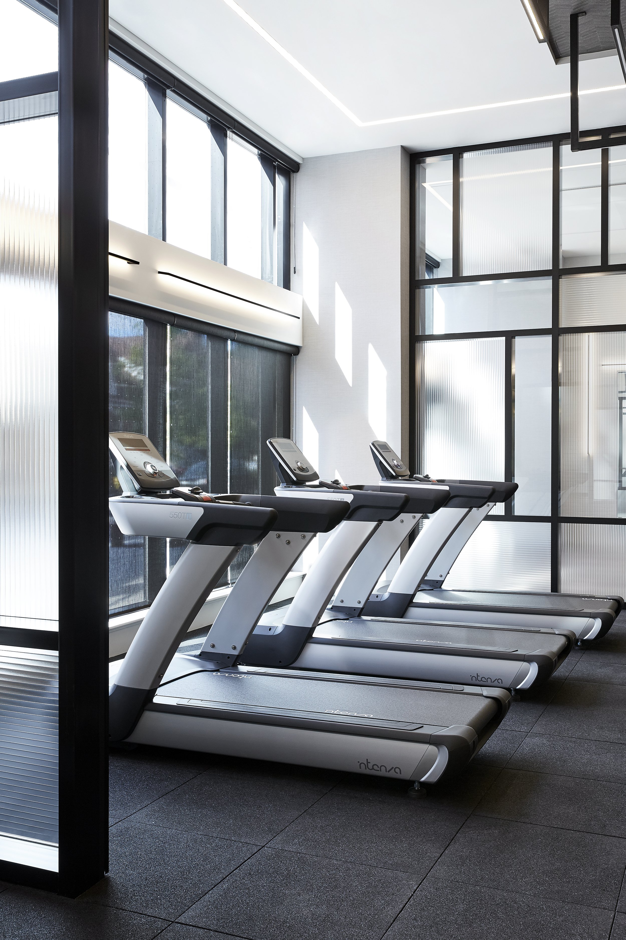 Treadmills in the  bright and spacious gym at Mattamy Homes - J. Davis Condominium, includes floor to ceiling large windows and black-framed glass walls.