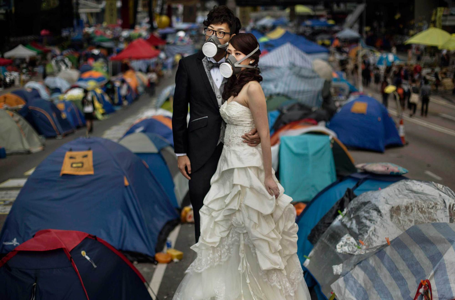 A newlywed couple wears gas masks while taking wedding photos beside pro-democracy demonstrators at the Admiralty protest site in Hong Kong. Source: Kevin Frayer/Getty Images. 