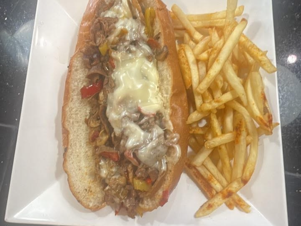 Phillycheese steak, peppers, onions, and melted cheese served with a side of French fries.