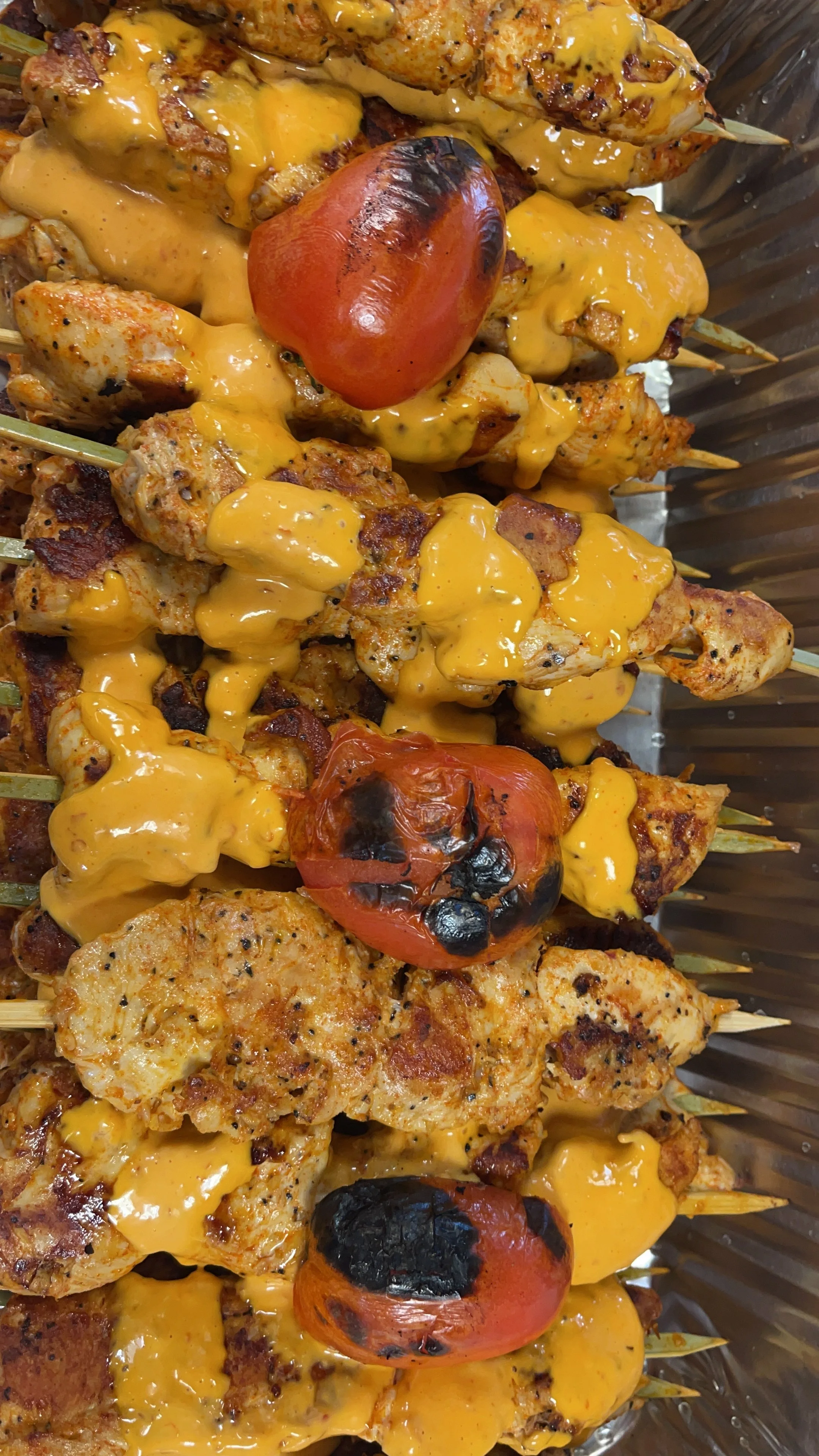 Close-up of grilled chicken skewers with special sauce and charred cherry tomatoes.
