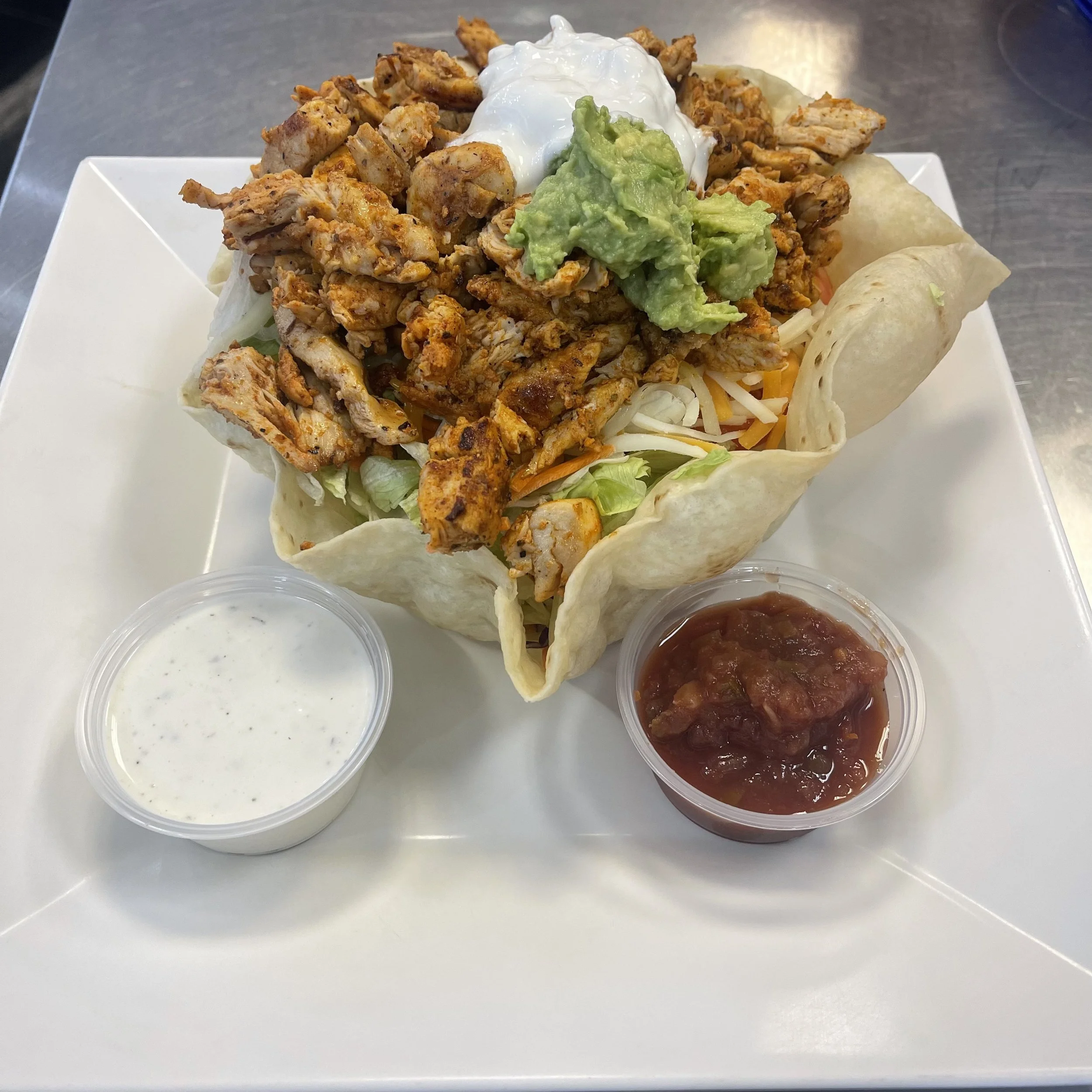 Chicken taco salad, guacamole, sour cream, shredded cheese, and taco shell, served with sides of salsa and sour cream in small cups.