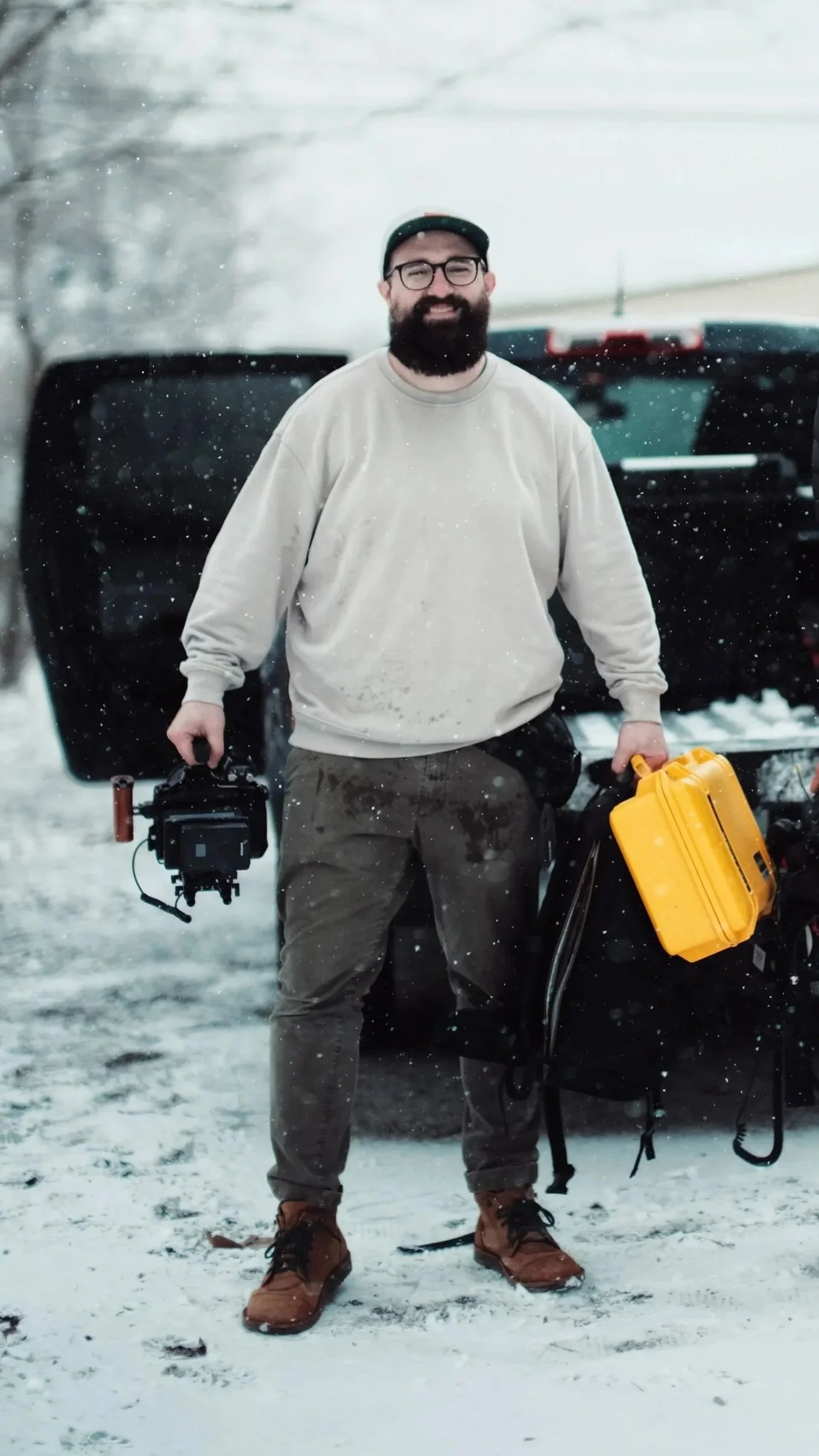 Zach Lucero, professional videographer, holding a Canon R5C cinema camera rig and yellow Pelican case on a snowy video production shoot.