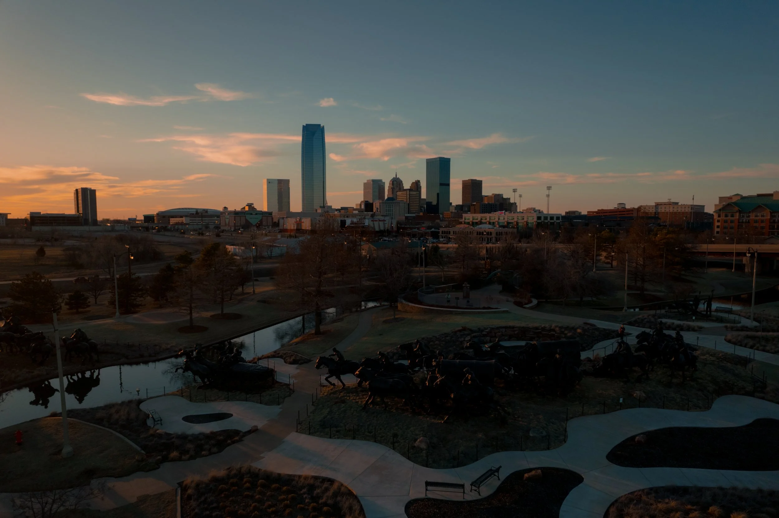 Drone photography of the Oklahoma City skyline at sunset overlooking the Oklahoma Land Run Monument - with downtown parks in the foreground