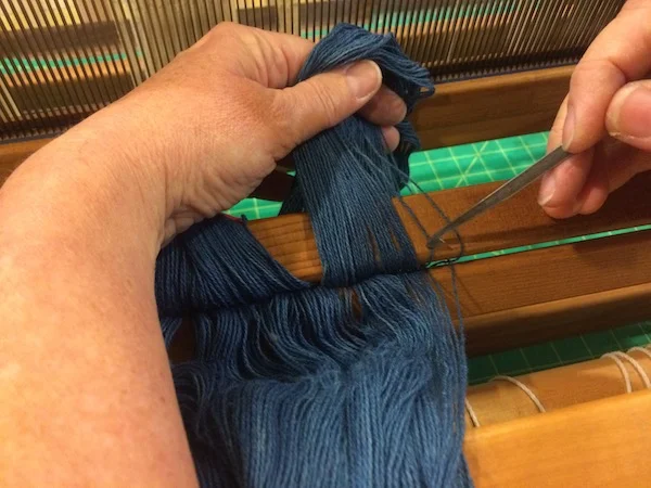 Beaming the warp threads by pulling them through the reed. 