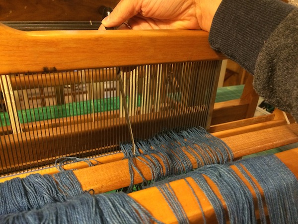  Pulling the warp threads through the reed.&nbsp; 