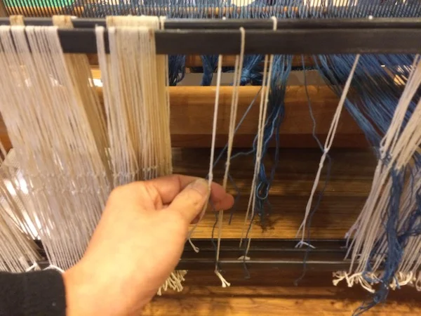 After we are finished threading the reed, we pull the indigo warp yarns through the homemade heddles. 