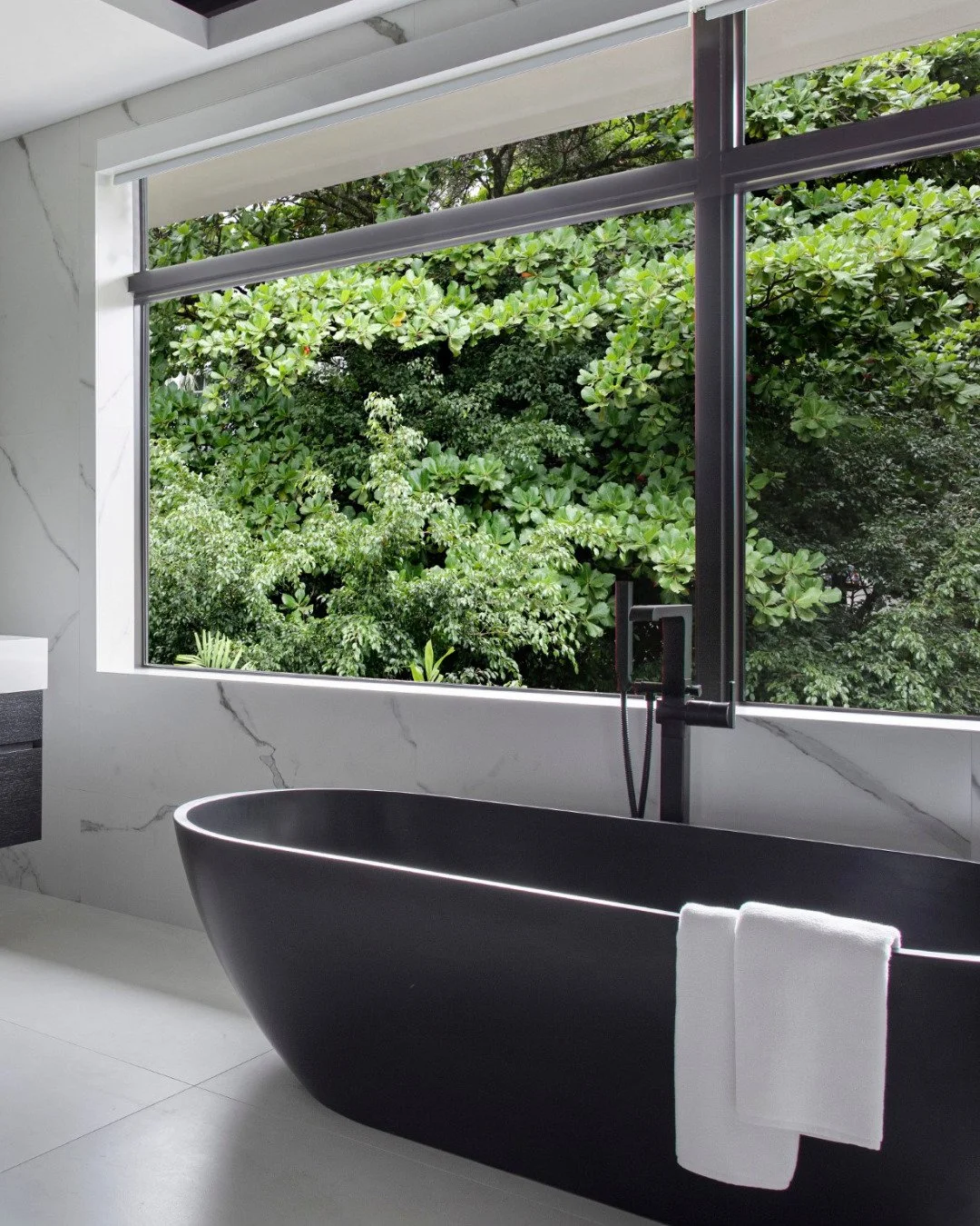 There was a very intentional contrast in this bathroom from the very beginning.

The softness of the marble, the natural light, and the greenery outside brought a sense of calm to the space, while the matte black tub and darker details added a strong
