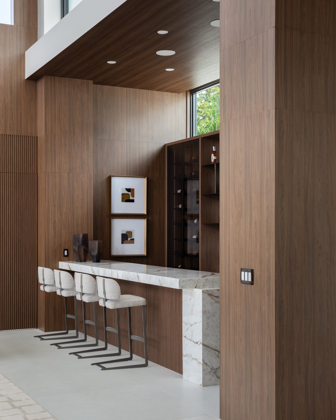 The wood carries through from the bar to the kitchen, giving the two spaces a familiar connection without making them feel the same.

At the bar, it wraps the walls and ceiling around a pale stone counter. In the kitchen, it sits alongside white cabi
