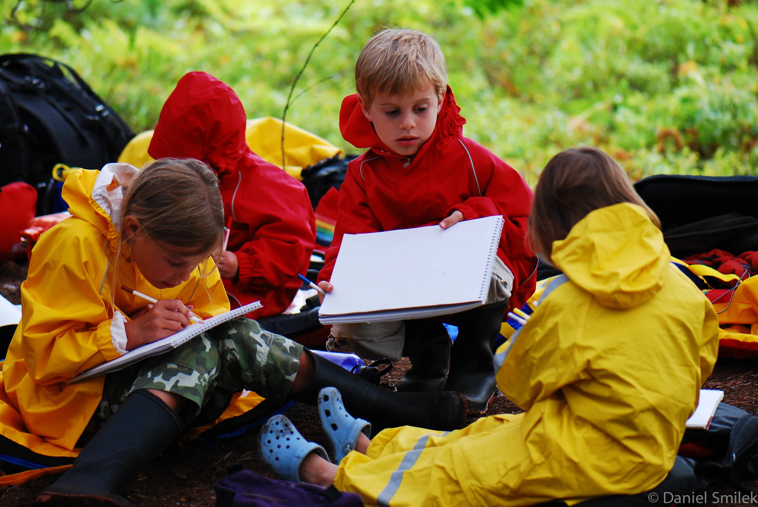 The kids drawing while sitting under a tarp.