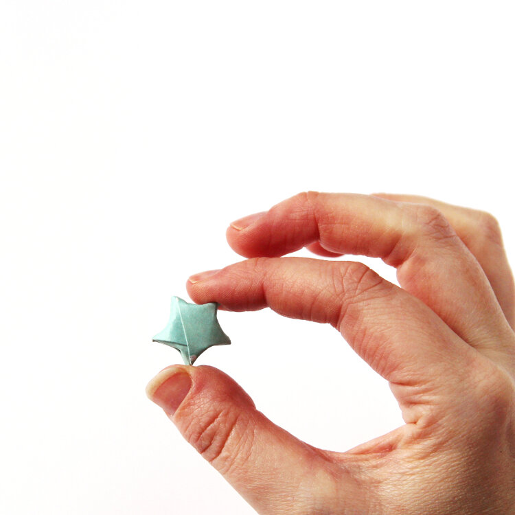 single origami lucky star being held between a finger and thumb
