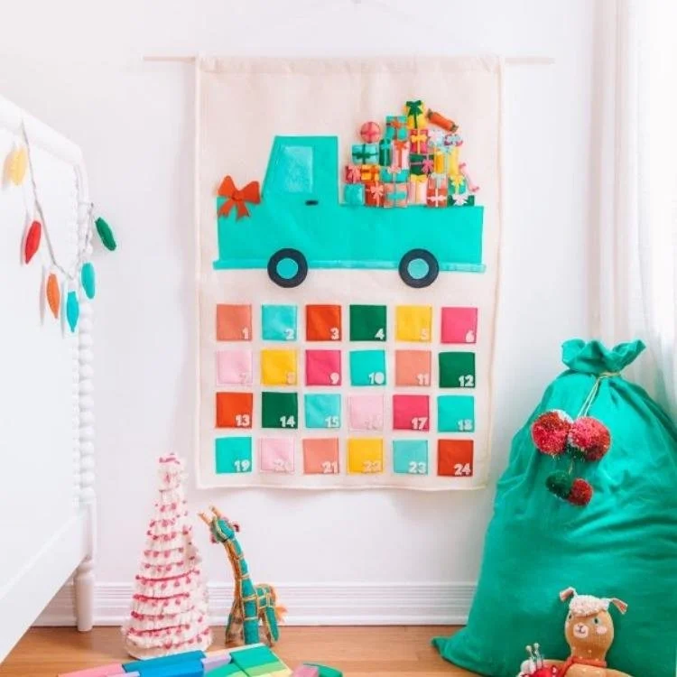 cream felt advent calendar with green felt truck filled with presents and pockets hanging on wall
