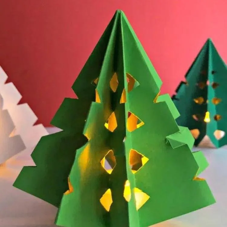 green folded paper tree with light shining through cut out shapes