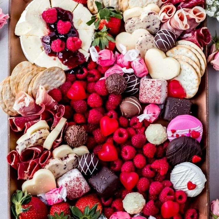 wooden board filled with meats, cheese, strawberries. raspberries and crackers