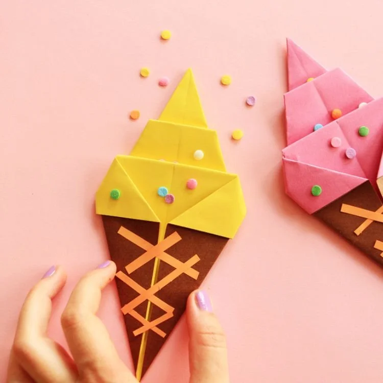 Hand holding origami ice cream cone with yellow ice cream.