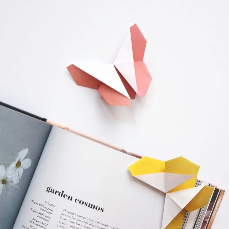 Peach and lemon origami butterfly bookmarks resting on book.