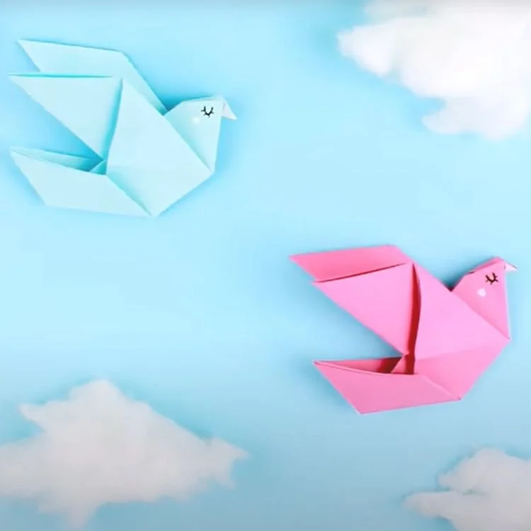 Pink and blue origami birds on blue background with cotton wool clouds.