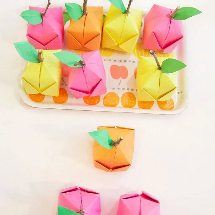 Pink, orange and yellow origami fruit on tray.