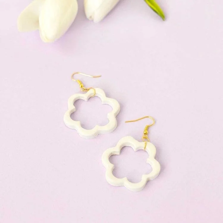 Flower shaped earrings on lilac background.