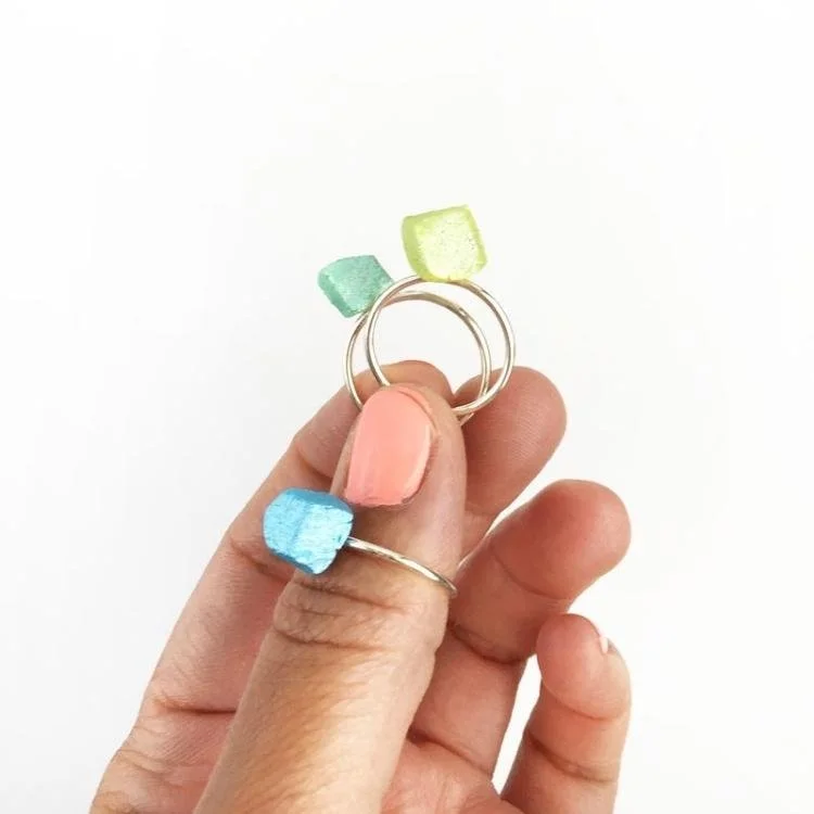 Hand holding two gold rings with pastel gems on top.