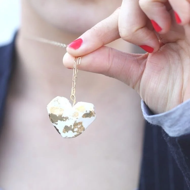 Hand holding up white and gold heart pendant.