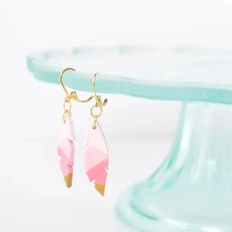 Pink feather shaped earrings hanging from the edge off blue glass cake stand.
