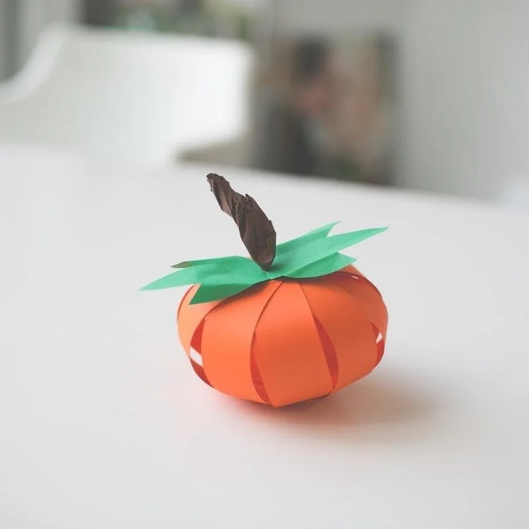 Mini orange paper pumpkin with green tissue paper leaves and stalk.
