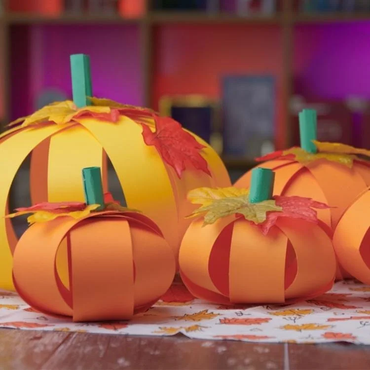 Orange paper pumpkins topped with orange leaves and green paper stalks.