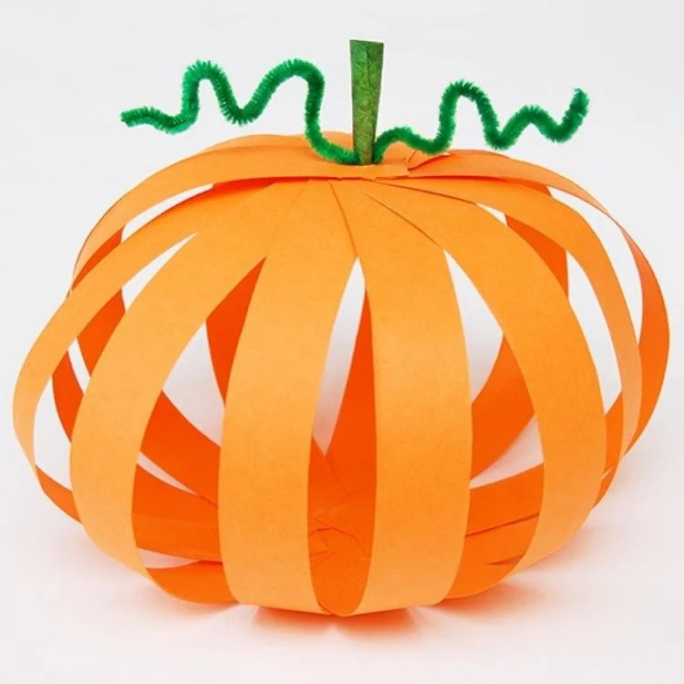 Paper pumpkin made out of orange paper strips with green pipe cleaner stalk.