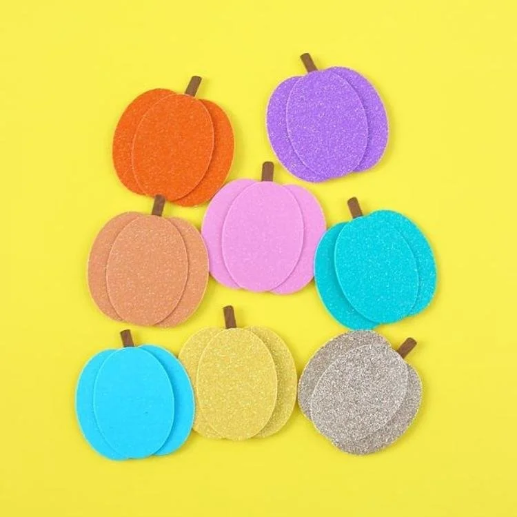 Paper pumpkins made out of glitter card on yellow background.