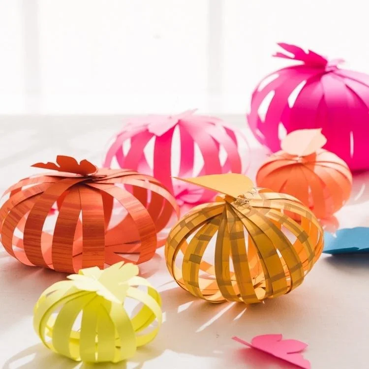 Paper strip pumpkins made out of bright orange yellow and pink paper.