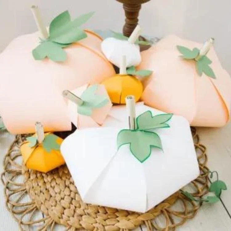White and pale orange paper pumpkins sitting on raffia placemat.