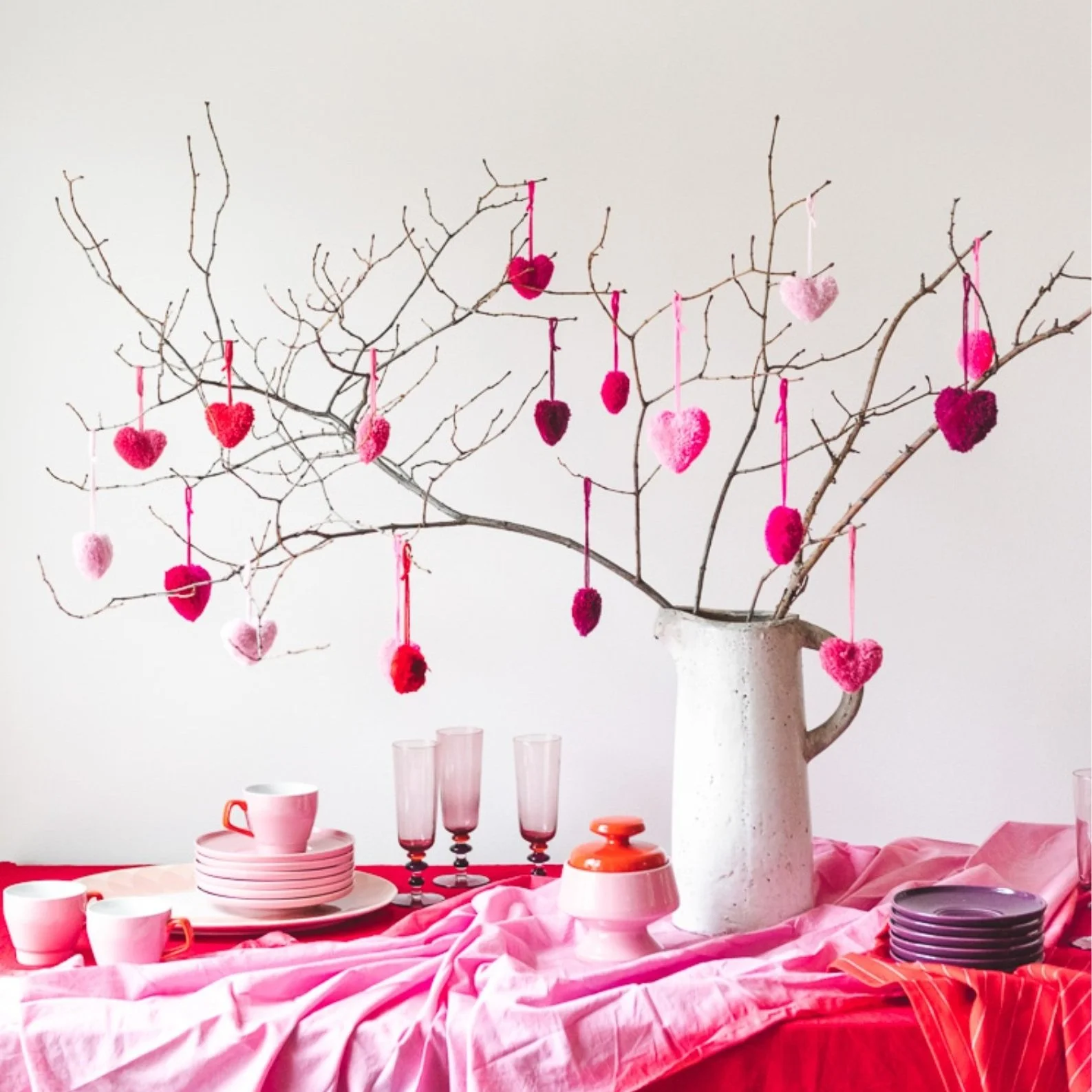 Heart shaped pom poms hanging on branches in jug.