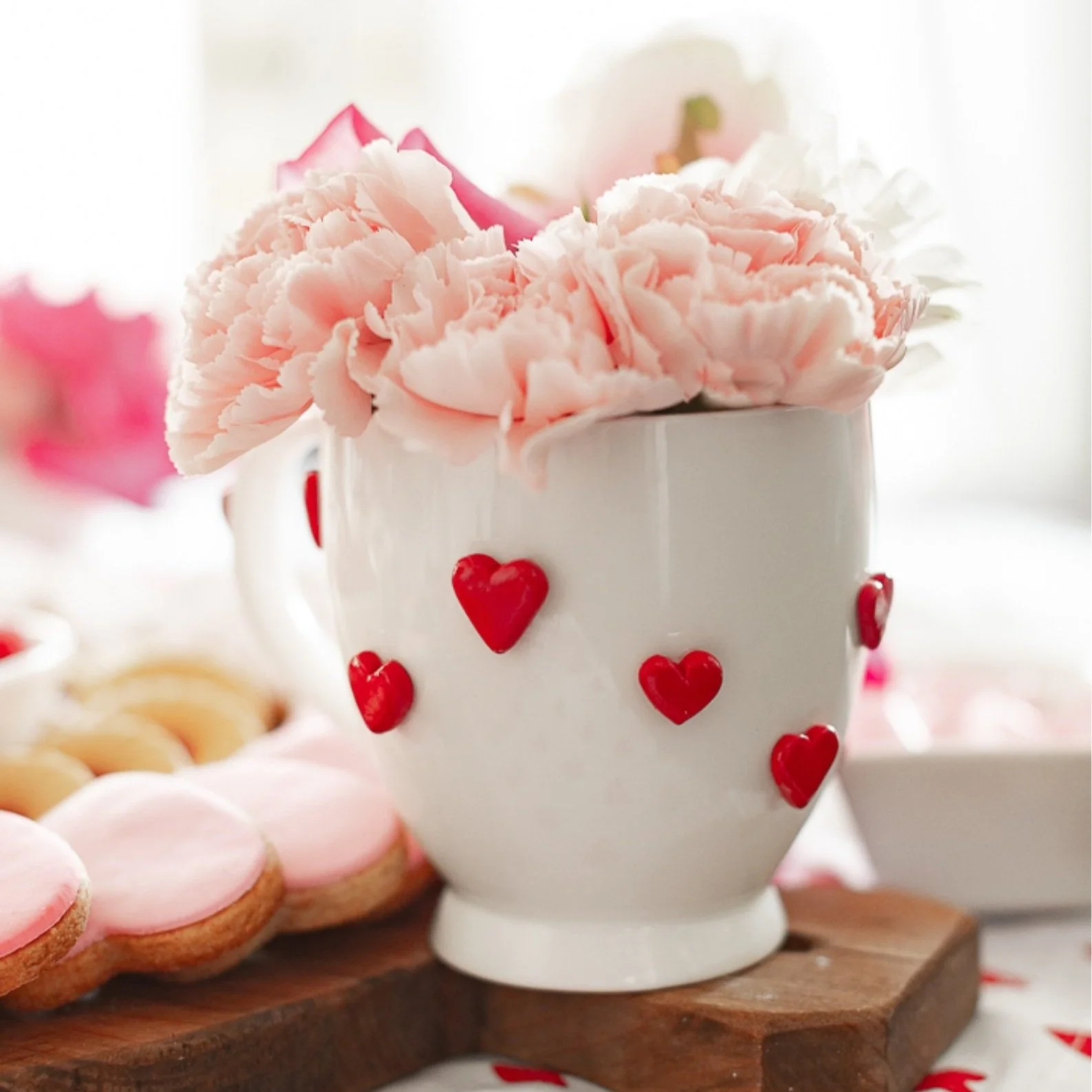 White mug covered in red hearts and filled with pink flowers.