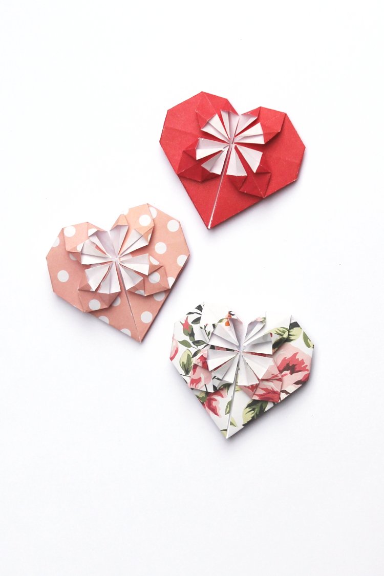 3 red and peach origami paper hearts on white background.