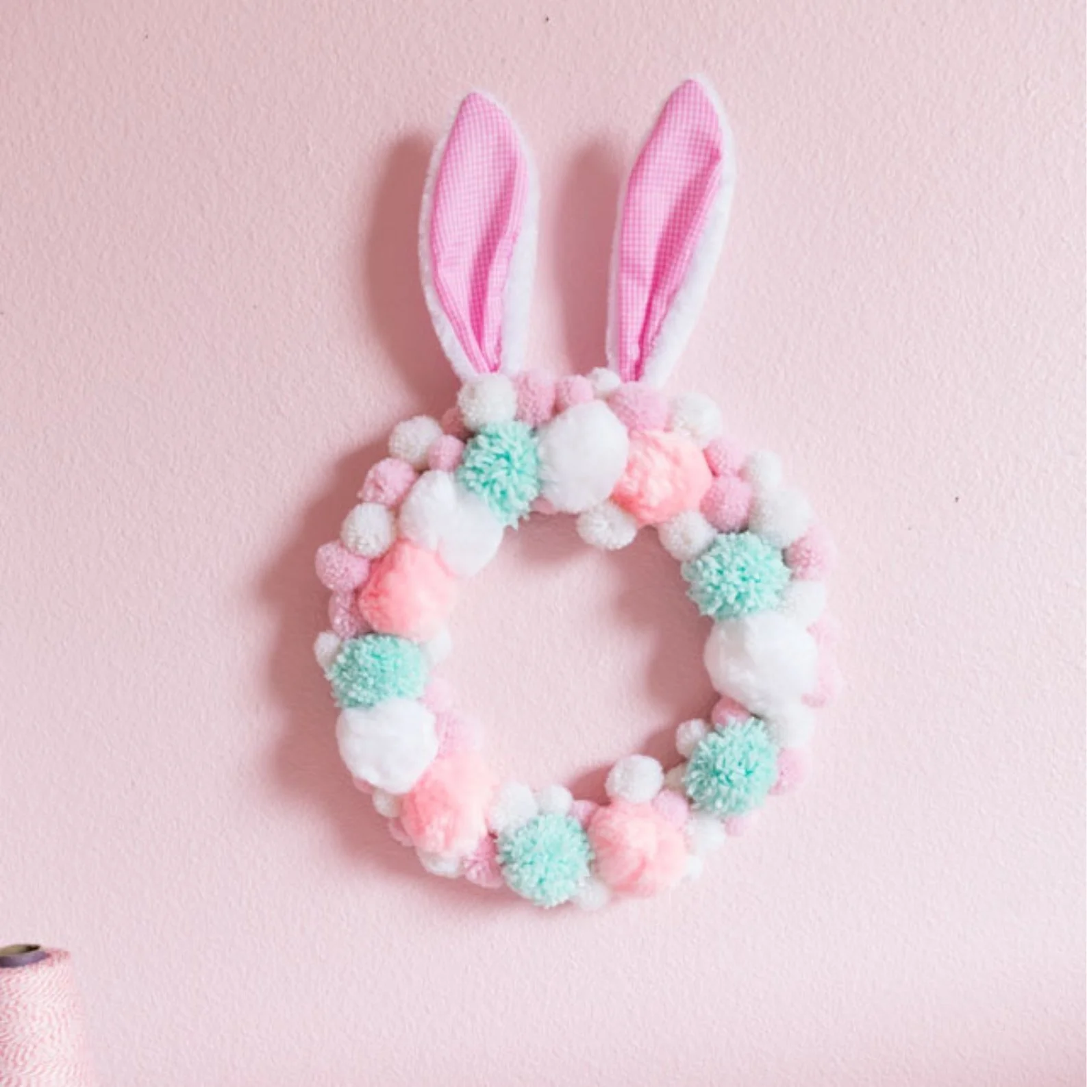 This pom-pom Easter bunny wreath is easy to make with a mix of yarn and craft pom-poms and a set of bunny ears.