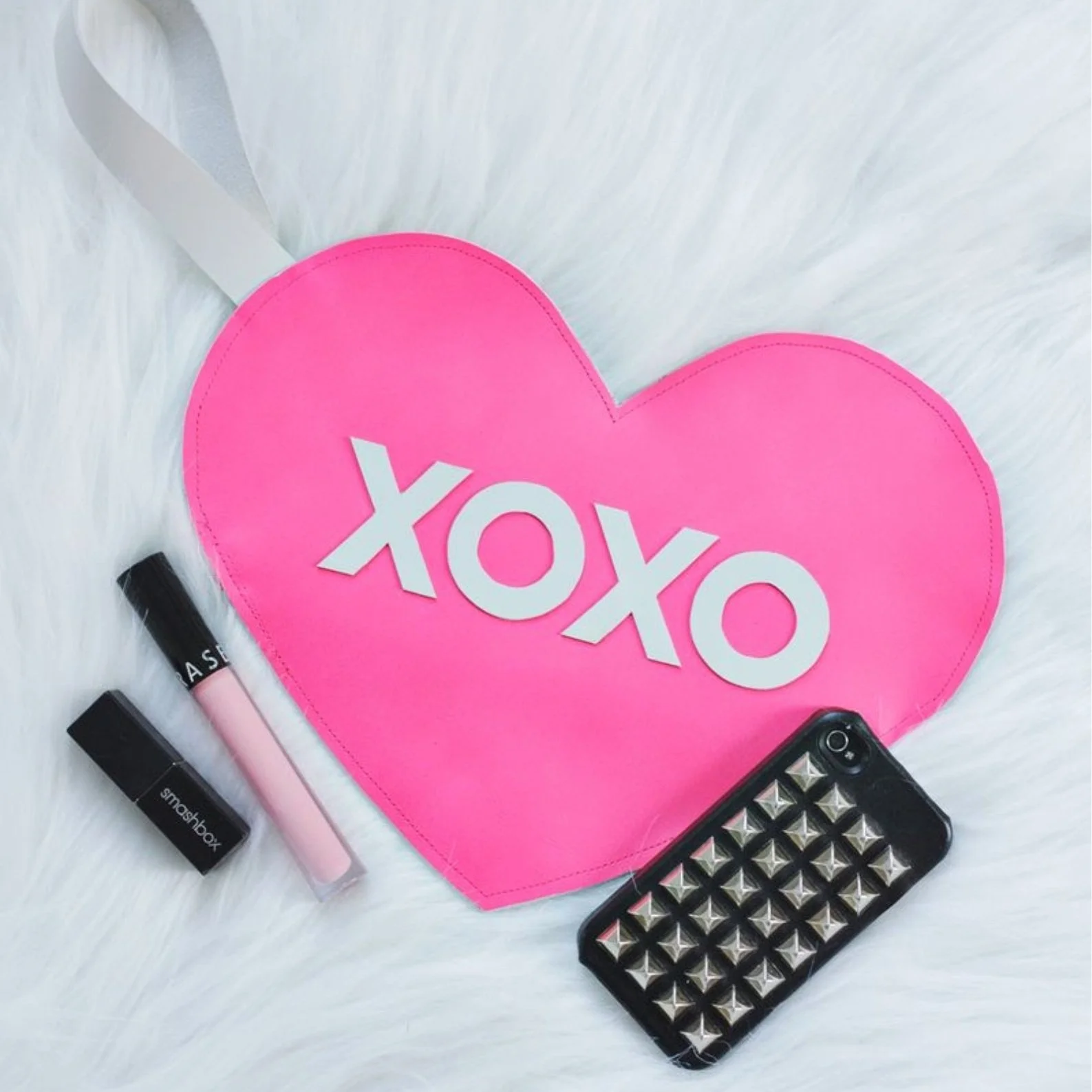 Pink heart shaped clutch bag on white fluffy rug.