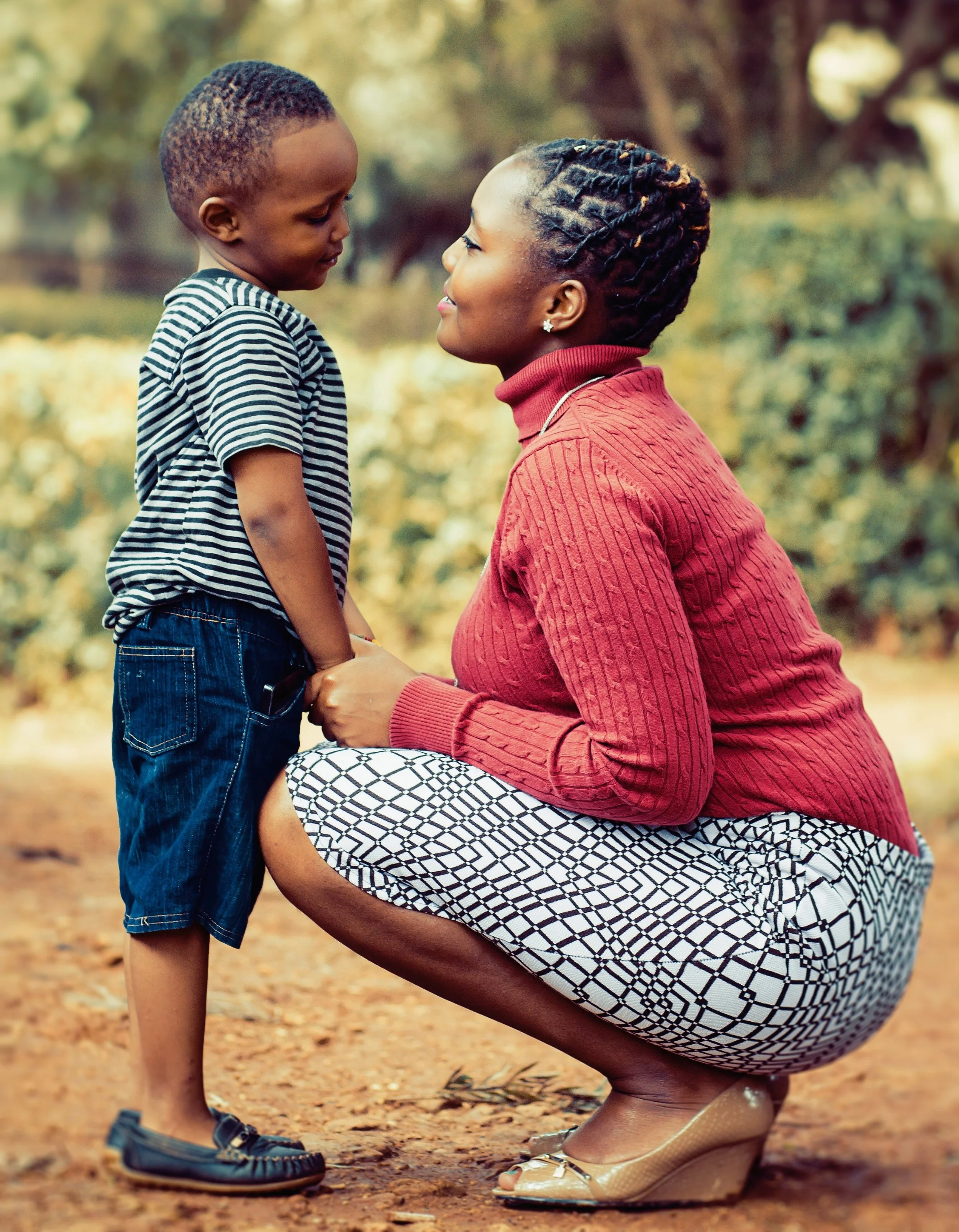 woman kneeling and holding a child’s hands
